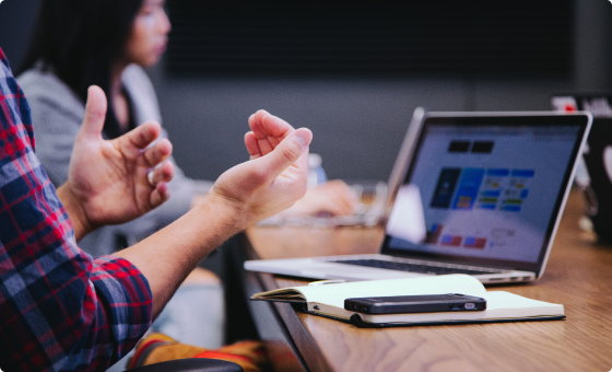 Hands gesturing over laptop and notebook at a meeting table